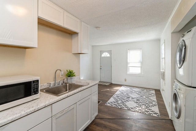 kitchen with stacked washer and clothes dryer, white microwave, dark wood-style floors, white cabinetry, and a sink