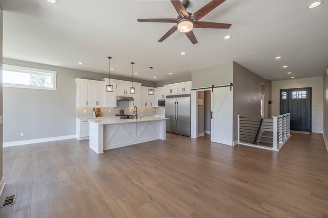 5009 148th Cir, Urbandale, IA 50323 - kitchen featuring stainless steel appliances, a barn door, light countertops, white cabinets, and an island with sink