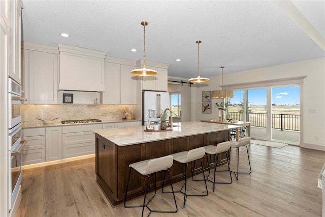 5027 NE Seneca Dr, Ankeny, IA 50021 - kitchen with white appliances, decorative backsplash, an island with sink, light wood-style floors, and recessed lighting