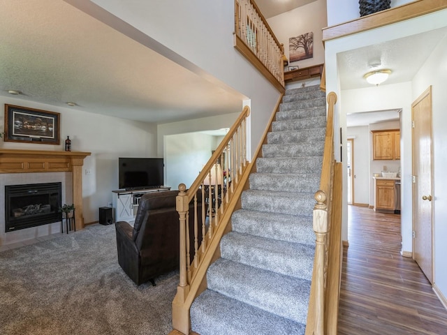 2917 SW Coves Dr, Ankeny, IA 50023 - staircase featuring baseboards, carpet flooring, a textured ceiling, a tile fireplace, and wood finished floors