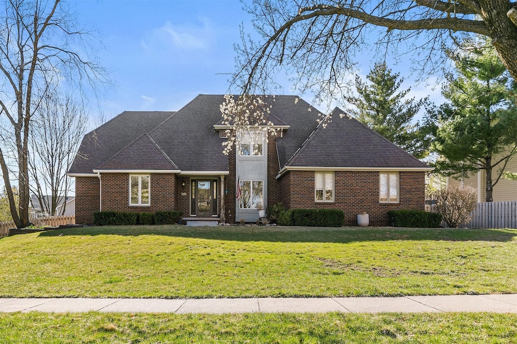 view of front facade with brick siding, roof with shingles, a front lawn, and fence