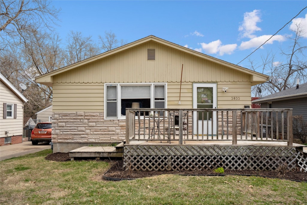 rear view of house with a yard, stone siding, and a wooden deck