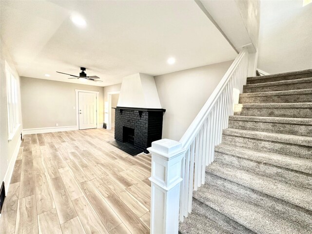 stairway featuring baseboards, a ceiling fan, a fireplace, recessed lighting, and wood finished floors