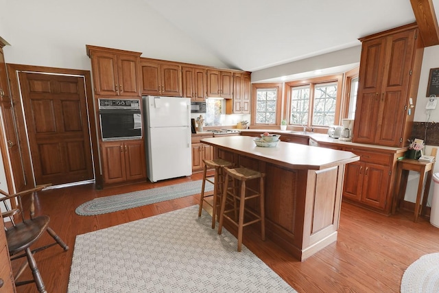 1113 Bruce Ln, Pella, IA 50219 - kitchen featuring light countertops, a breakfast bar, light wood-style floors, black appliances, and lofted ceiling