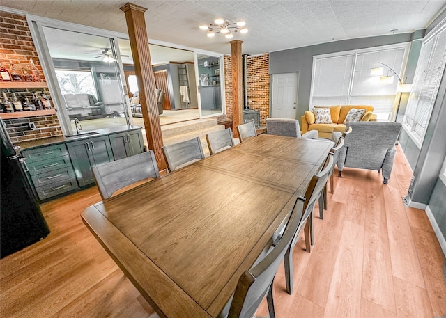 1009 198th Pl, Pella, IA 50219 - dining room featuring ornate columns, light wood finished floors, brick wall, ceiling fan, and a chandelier