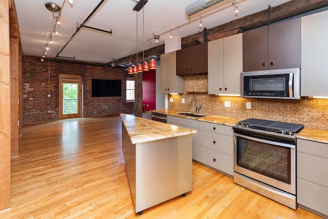 301 E Court Ave Unit 203, Des Moines, IA 50309 - kitchen featuring track lighting, appliances with stainless steel finishes, brick wall, light wood-style floors, and open floor plan