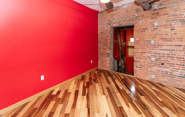 301 E Court Ave Unit 203, Des Moines, IA 50309 - spare room featuring wood-type flooring, a ceiling fan, and brick wall