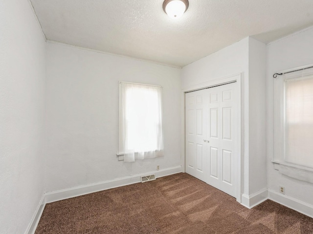 unfurnished bedroom featuring dark carpet, baseboards, multiple windows, and a closet