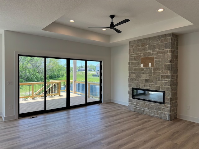 1112 2nd St NE, Altoona, IA 50009 - unfurnished living room with a raised ceiling, wood finished floors, a ceiling fan, a fireplace, and baseboards