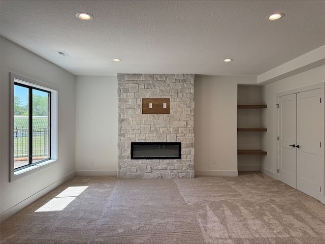1112 2nd St NE, Altoona, IA 50009 - unfurnished living room with carpet floors, a textured ceiling, a stone fireplace, recessed lighting, and baseboards