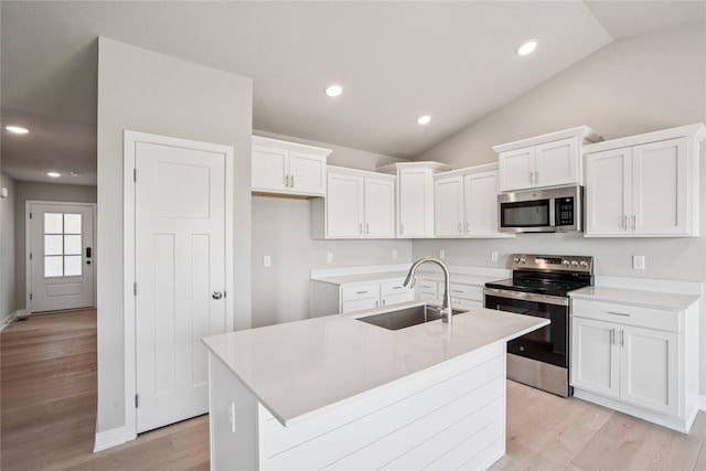 4413 NW Olivia Ln, Ankeny, IA 50023 - kitchen featuring stainless steel appliances, lofted ceiling, white cabinets, an island with sink, and light wood finished floors