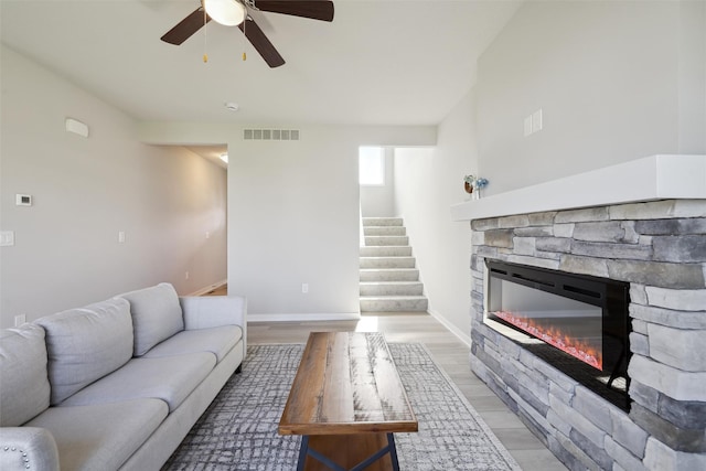 1715 Willow Ct, Norwalk, IA 50211 - living area featuring a stone fireplace, visible vents, a ceiling fan, light wood-style floors, and stairs