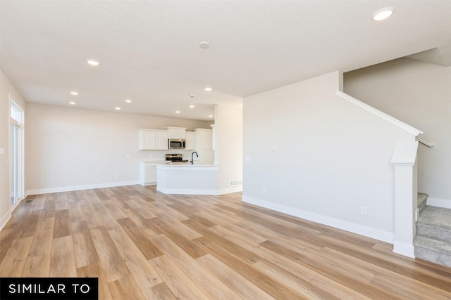 6511 NE George Ave, Pleasant Hill, IA 50327 - unfurnished living room with light wood-style floors, stairs, recessed lighting, baseboards, and a sink