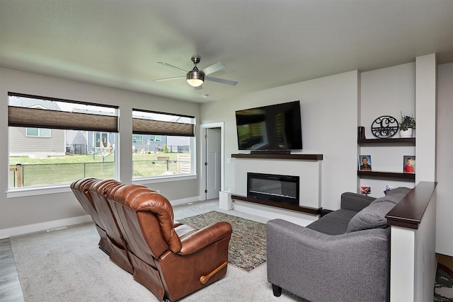 living room with visible vents, ceiling fan, a glass covered fireplace, and baseboards