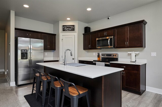 kitchen featuring dark brown cabinets, appliances with stainless steel finishes, a sink, light wood finished floors, and baseboards