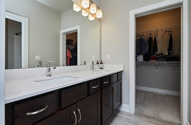 bathroom featuring wood finished floors, vanity, baseboards, and a walk in closet