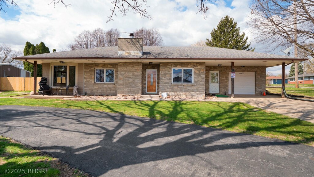 ranch-style home featuring driveway, stone siding, a front yard, a garage, and a shingled roof