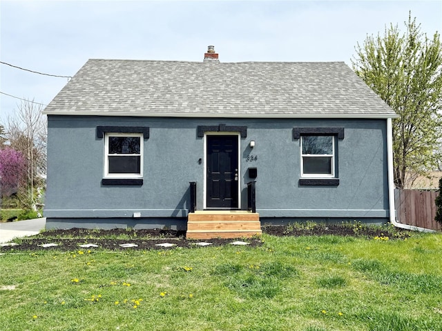 bungalow-style home with a chimney, fence, a front lawn, entry steps, and roof with shingles