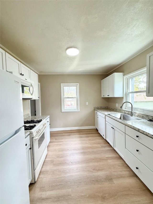kitchen with a sink, a textured ceiling, white appliances, a healthy amount of sunlight, and light wood finished floors