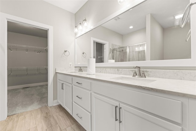 full bath featuring a sink, a walk in closet, a shower stall, and double vanity