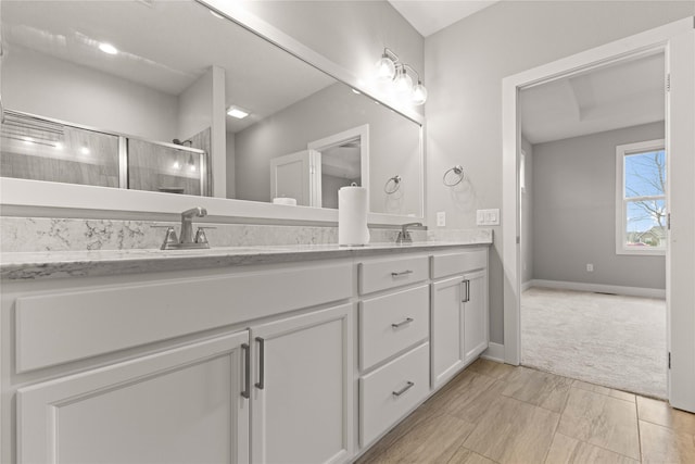 full bath featuring a sink, baseboards, a shower stall, and double vanity