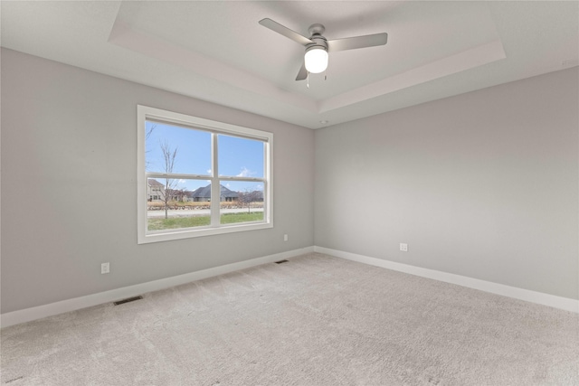 empty room featuring a tray ceiling, baseboards, carpet, and visible vents