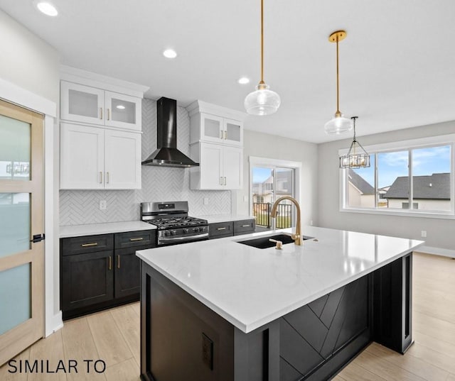 kitchen featuring stainless steel range with gas stovetop, wall chimney range hood, white cabinetry, a sink, and backsplash