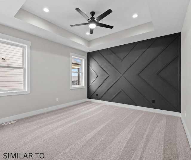 spare room with ceiling fan, a tray ceiling, visible vents, carpet floors, and baseboards