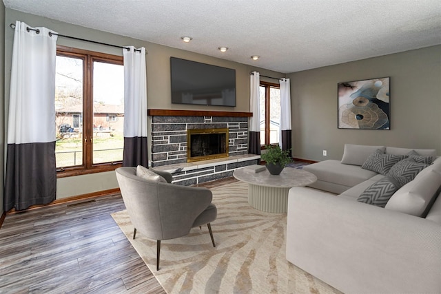 living area featuring a textured ceiling, baseboards, recessed lighting, wood finished floors, and a stone fireplace