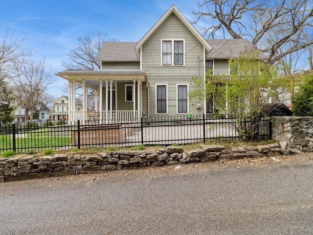 farmhouse inspired home with roof with shingles, covered porch, and a fenced front yard