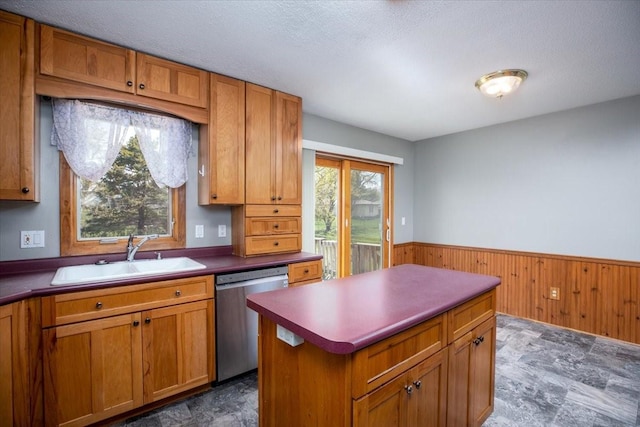 kitchen featuring dishwasher, a sink, brown cabinetry, wainscoting, and wood walls
