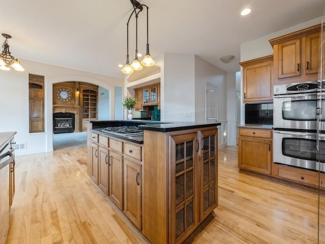 2705 147th St, Urbandale, IA 50323 - kitchen featuring appliances with stainless steel finishes, light wood-style floors, brown cabinetry, a fireplace, and a center island