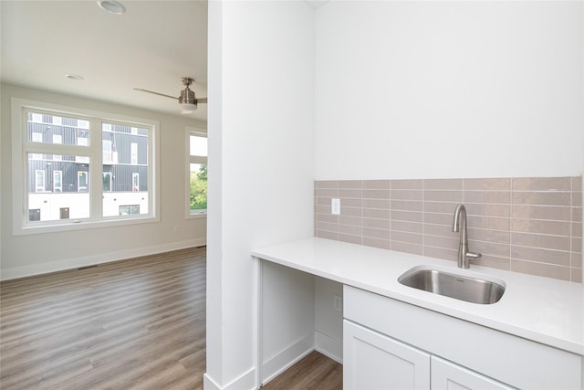 kitchen with baseboards, light wood-type flooring, light countertops, decorative backsplash, and a sink