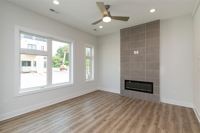 unfurnished living room featuring a tile fireplace, visible vents, baseboards, and wood finished floors