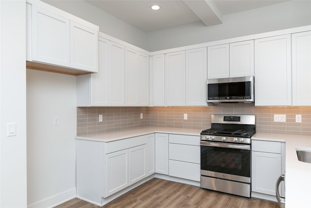 kitchen with tasteful backsplash, light countertops, appliances with stainless steel finishes, and light wood finished floors