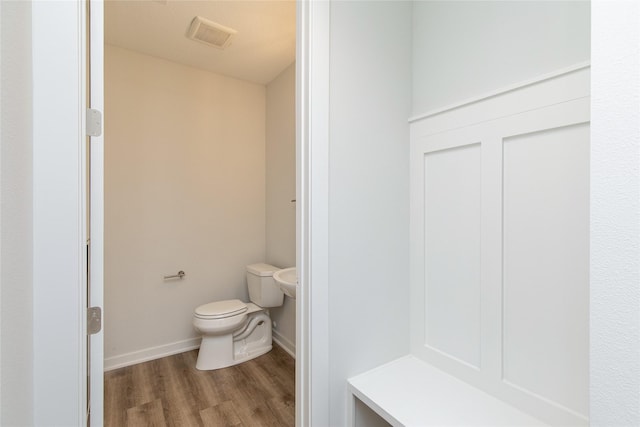 bathroom with toilet, wood finished floors, baseboards, and visible vents