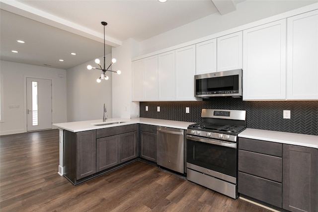 kitchen with dark wood-type flooring, a peninsula, a sink, stainless steel appliances, and decorative backsplash