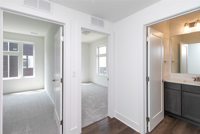 hallway with a sink, dark wood-style flooring, baseboards, and visible vents