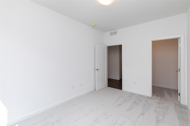 unfurnished bedroom with a walk in closet, baseboards, visible vents, and carpet floors