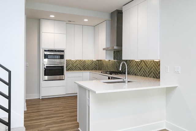 209 Maple St, Des Moines, IA 50309 - kitchen featuring stainless steel double oven, wall chimney exhaust hood, decorative backsplash, a sink, and wood finished floors