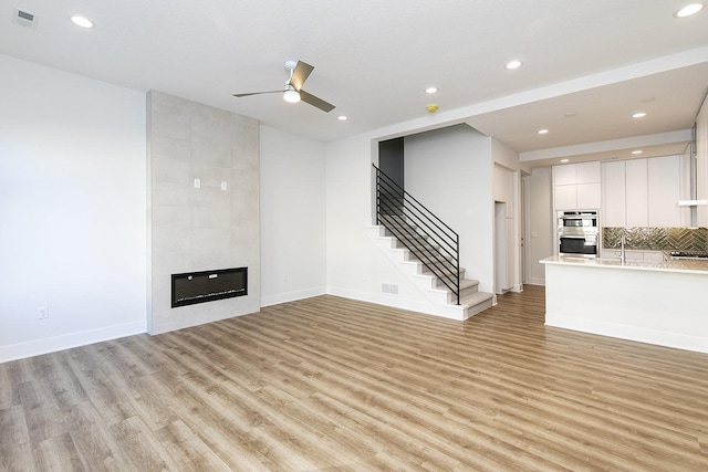 209 Maple St, Des Moines, IA 50309 - unfurnished living room with visible vents, a ceiling fan, a fireplace, stairway, and light wood-style flooring