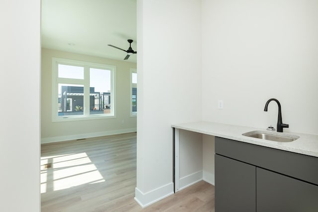 bar with light wood-type flooring, ceiling fan, a sink, and baseboards