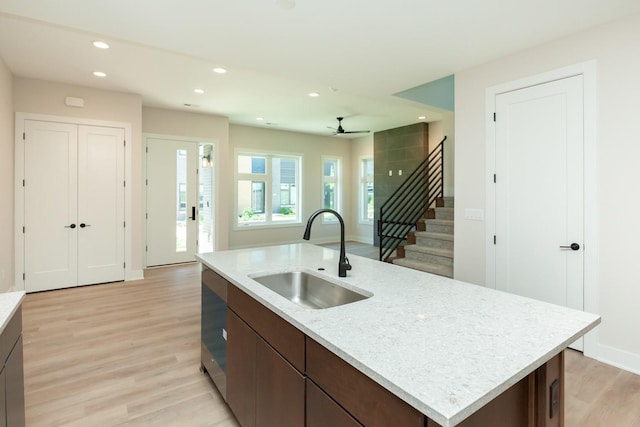 kitchen with a sink, light wood-type flooring, a kitchen island with sink, dark brown cabinetry, and recessed lighting