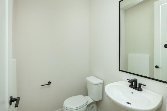 half bath featuring toilet, a sink, and baseboards