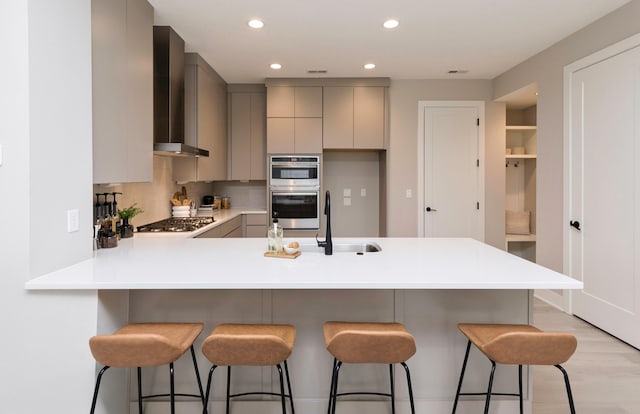 820 E 2nd St, Des Moines, IA 50309 - kitchen featuring a peninsula, wall chimney range hood, gray cabinets, light countertops, and stainless steel appliances
