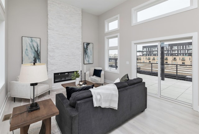 820 E 2nd St, Des Moines, IA 50309 - living room featuring light wood-style flooring, a stone fireplace, visible vents, a high ceiling, and baseboards