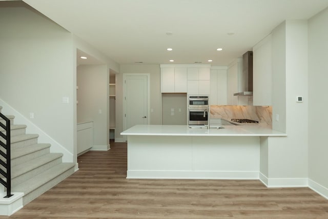 822 E 2nd St, Des Moines, IA 50309 - kitchen featuring wall chimney range hood, a peninsula, light countertops, gas cooktop, and double oven