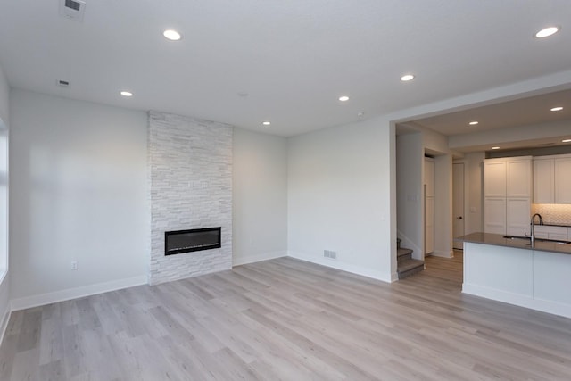 unfurnished living room with recessed lighting, stairway, light wood-style flooring, visible vents, and a sink