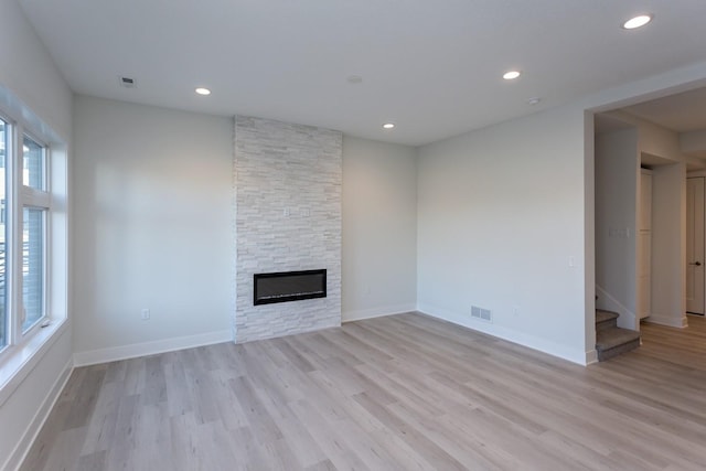 unfurnished living room with visible vents, a stone fireplace, stairway, and light wood-style floors