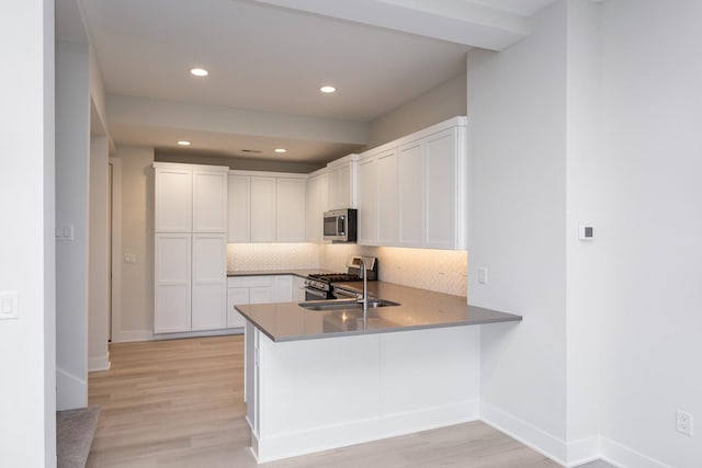 kitchen with tasteful backsplash, a sink, light wood finished floors, white cabinetry, and stainless steel appliances